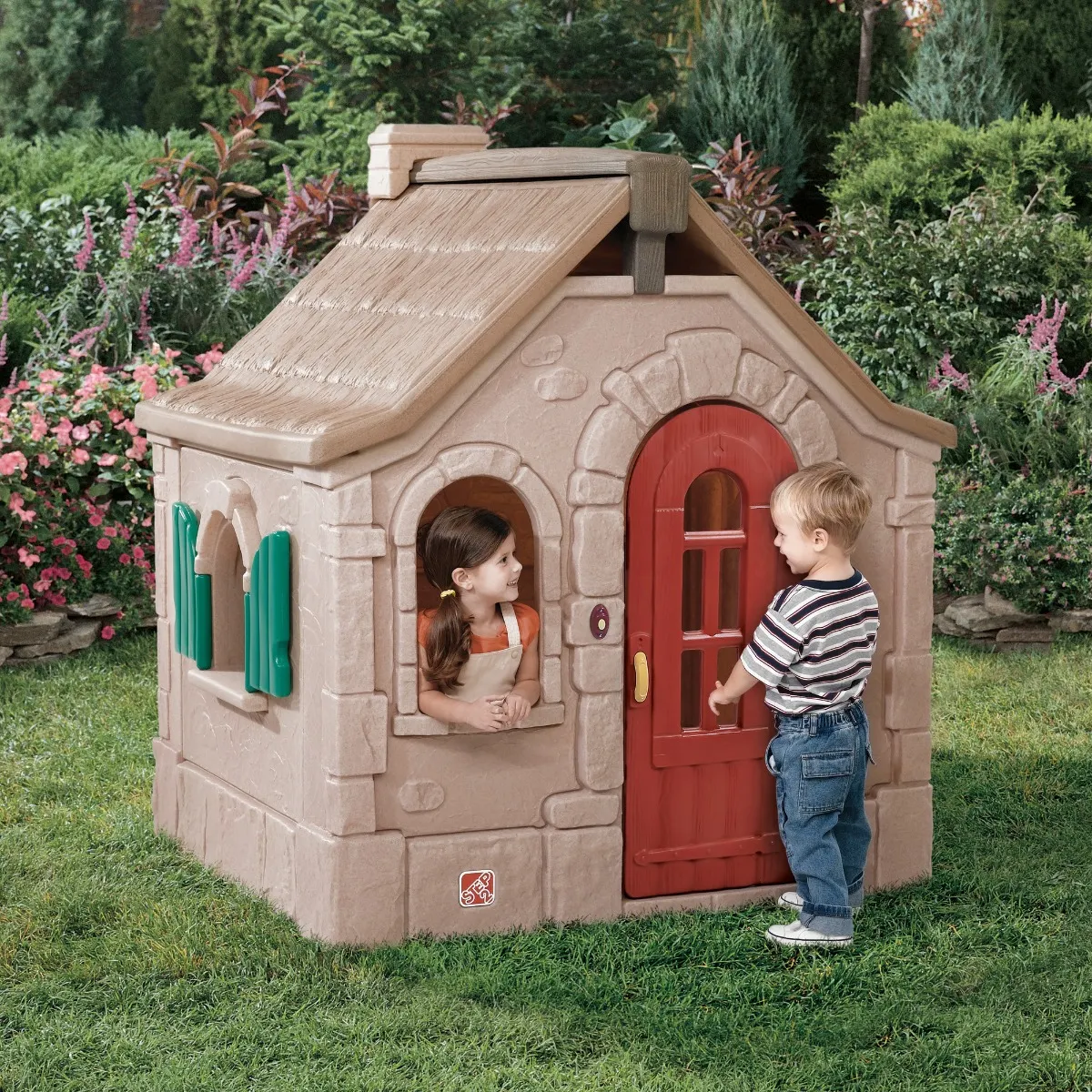 boy and girl playing with a plastic playhouse in the garden