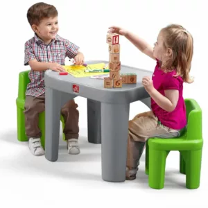 A boy and a girl sit at a gray Step2 Mighty My Size Table with two green chairs, playing with colorful blocks and a drawing.