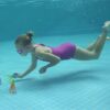 girl wearing swimming goggles underwater in a pool playing with a squid dive toy