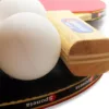 two table tennis bats and two white balls close-up view