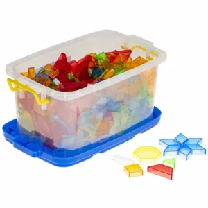 A clear plastic storage bin with a blue base and yellow handles, filled with colorful transparent pattern blocks in various geometric shapes. Several blocks are arranged outside the bin, forming patterns and shapes.