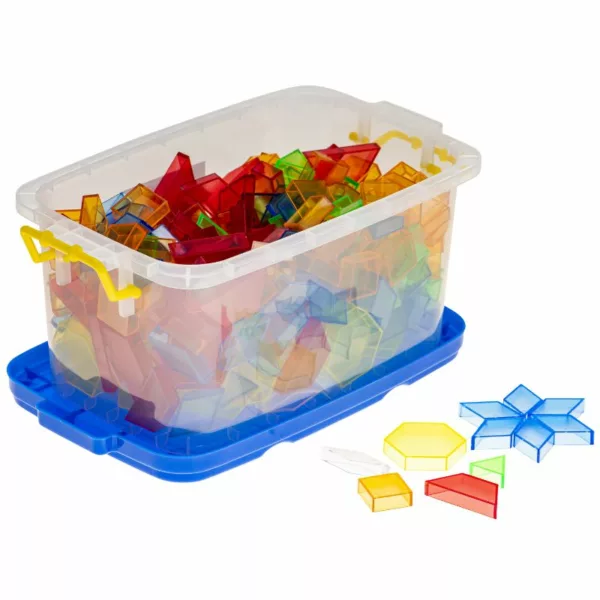 A clear plastic storage bin with a blue base and yellow handles, filled with colorful transparent pattern blocks in various geometric shapes. Several blocks are arranged outside the bin, forming patterns and shapes.