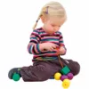 A young child sitting on the floor, focused on threading colorful giant lacing beads onto an orange lace, wearing a striped shirt and dark pants.