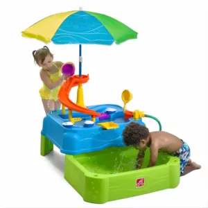 Two children playing with the Step2 Waterpark Wonders Two-Tier Water Table, which includes a slide, an umbrella, and a lower basin for splashing.