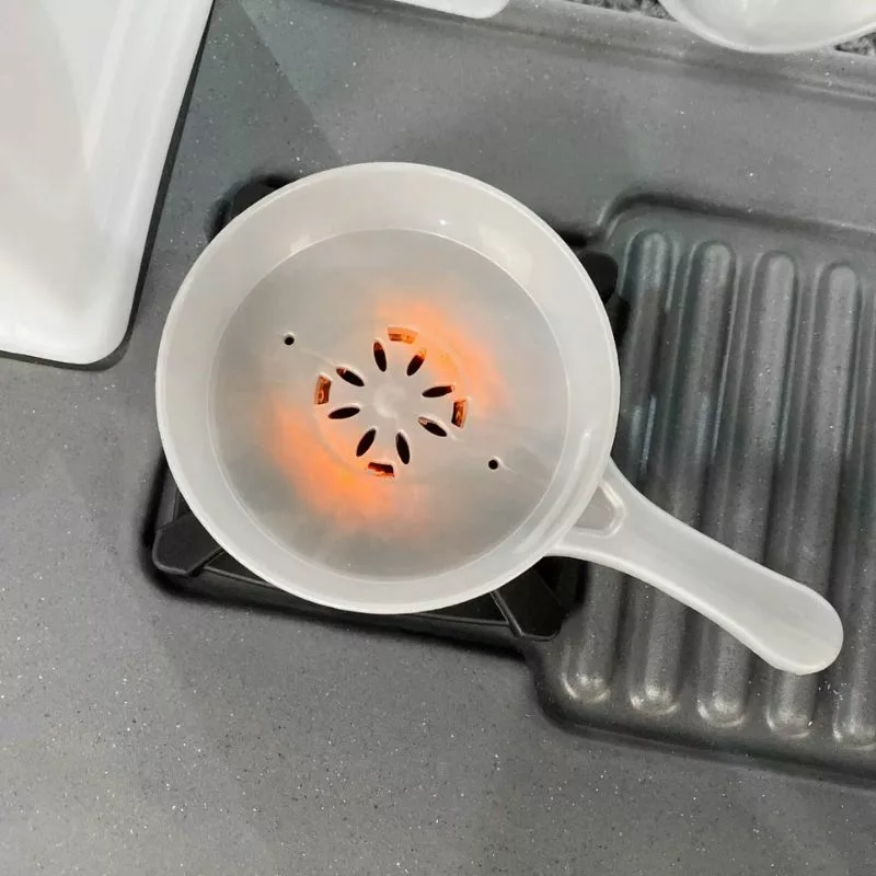 A close-up of a toy kitchen stove with a translucent white plastic pan on a burner. An orange light is glowing from underneath the pan, simulating a hot burner. The toy stove is part of a Step2 Cooking Time Kitchen playset.