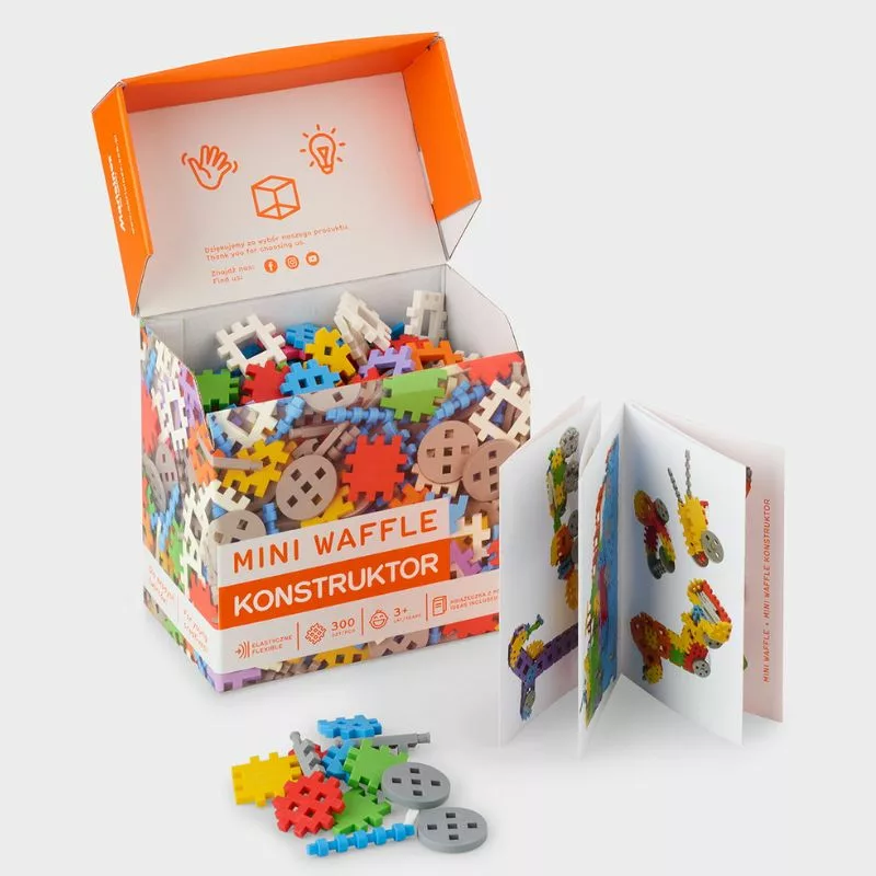 A bright orange and white box of "Marioinex Mini Waffle Constructor 300" building blocks, showing multicolored pieces (red, blue, white, orange) spilling out of the top. The box also indicates features like a washing bag, booklet with ideas, and a 4+ age rating.